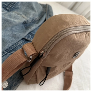 Detail of khaki nylon crescent bag with silver metallic logo and pleated texture