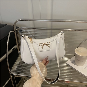White patent leather baguette shoulder bag with gold bow buckle in a lifestyle setting