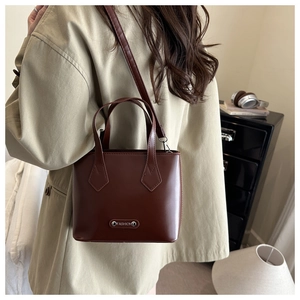 Detailed view of brown leather bucket bag with metal FASHION emblem on model