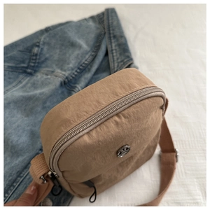 Detailed macro view of khaki nylon crossbody bag with silver M logo and metal zipper