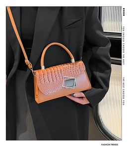 Detail of a brown faux crocodile texture crossbody bag with a geometric metal buckle