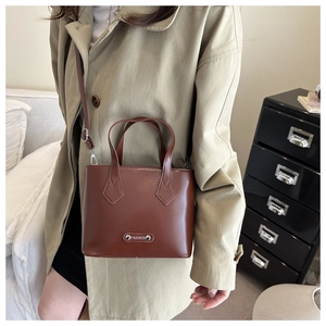 Detail of dark brown leather bucket bag showing silver Fashion plaque and adjustable strap