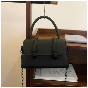 Détail du sac en cuir noir mat avec bandoulière chaîne sur un support en bois