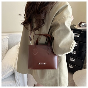 Detail of a dark brown vintage bucket bag with metal nameplate and adjustable strap