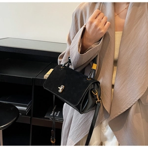 Detail of black suede and leather crossbody bag with gold buckle on trench coat