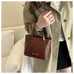 Close-up of caramel leather mini tote bag with silver fashion plaque on khaki trench coat