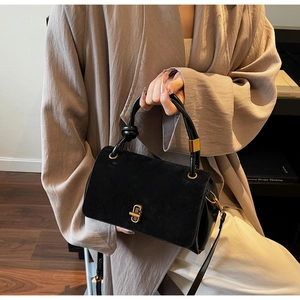 Close-up of black suede and smooth leather handbag with metal lock and knot detail