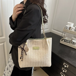 Chic beige straw tote bag with green leather patch and bow detail shown on a model