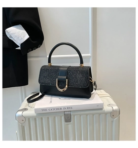 Detail view of black glitter flap handbag with gold D-buckle on a white suitcase