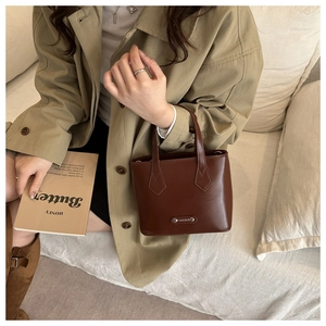 Detail of dark brown leather handbag with a metal fashion tag and firm double handles