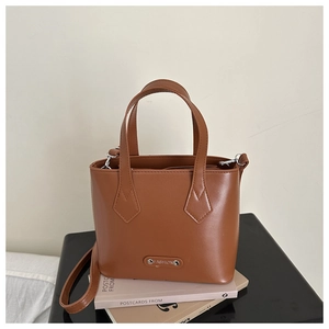 Close-up of brown faux leather bucket bag with silver Fashion plaque on black surface