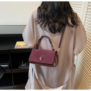 Detail of burgundy suede and leather handbag featuring a gold twist lock and woven handle