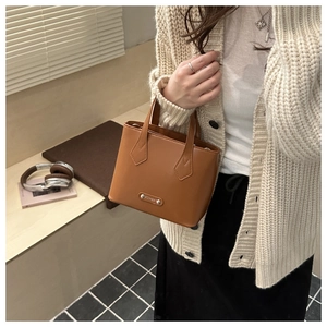 Close-up of brown PU leather bucket bag with metal fashion tag on a wooden bench