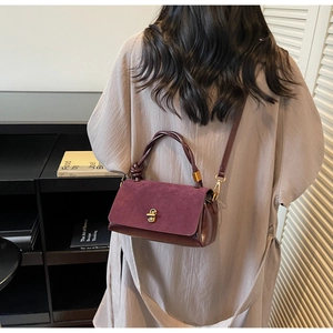 Detail of burgundy suede and leather handbag with a unique knotted handle and gold clasp