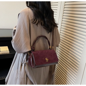 Detail of burgundy suede leather handbag with metal lock and knot handle design