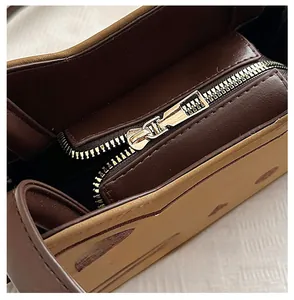 Detail view of a smooth gold metal zipper on a brown patchwork kids shoulder bag