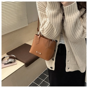 Close-up of brown leather bucket bag with fashion metal plate on beige sweater