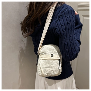 Detail view of cream nylon crossbody bag with textured fabric and metallic logo detail