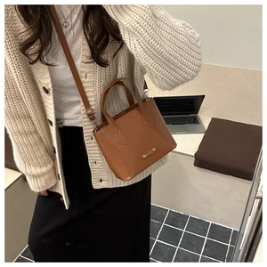 Brown faux leather bucket bag featuring a rectangular metal fashion tag and detachable strap