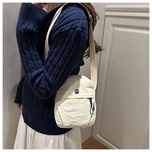 Detail of white nylon crossbody bag featuring a round metal logo and pleated texture finish