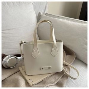 Detail of white mini bucket bag with metal fashion tag on a soft lifestyle background