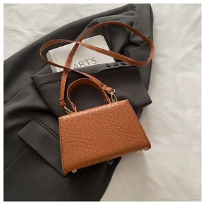 Détails du sac à main marron tressé avec clous dorés posé sur un blazer gris chic