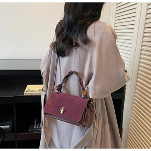 Detail of burgundy suede tote with knotted handle and metal twist lock on model
