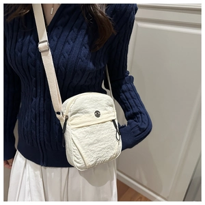 Detail of off-white pleated crossbody bag featuring a circular metal logo and adjustable strap