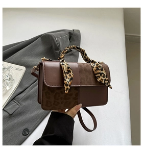 Close-up of brown leather handbag with leopard print accents and silk scarf handle