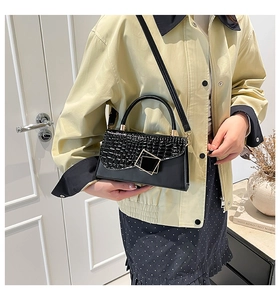 Close-up of black crocodile pattern flap bag with golden buckle and sleek shoulder strap