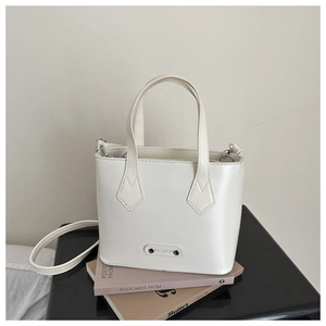 Close-up of white leather bucket bag with FASHION metal tag and diamond stitching