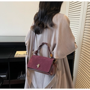 Side view of a burgundy suede handbag featuring a retro gold twist lock and knotted handle