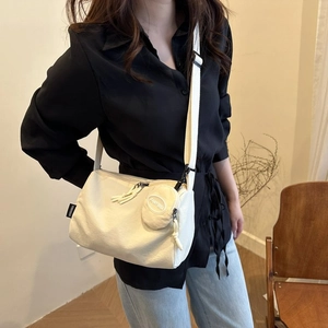 Détail d'un sac bandoulière en nylon crème avec étiquette de marque et pochette ronde