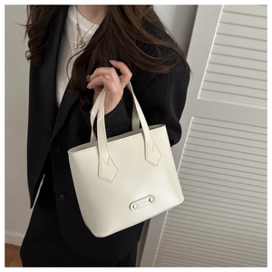 Detail view of cream white trapezoid tote bag with fashion metal plaque held by hand