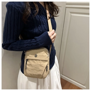 Detail of beige wrinkled nylon crossbody bag showing the zipper and metal logo