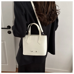 Detail of a creamy white bucket bag with FASHION metal tag and slim strap on model