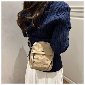 Detail of beige nylon crossbody bag featuring pleated texture and circular metal logo