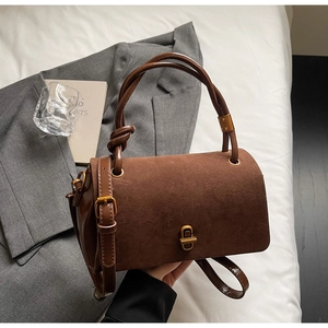 Detail of suede crossbody bag with gold twist-lock closure on casual white bedding