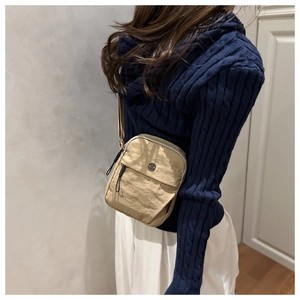 Side view of khaki pleated nylon crossbody bag with circular metal logo on a model