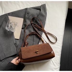 Detail of a brown faux leather crossbody bag with metallic lock on a grey suit jacket