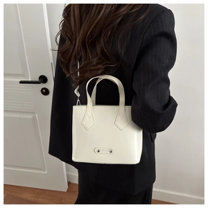 Detailed view of a white leather tote bag worn with a black striped blazer for daily style