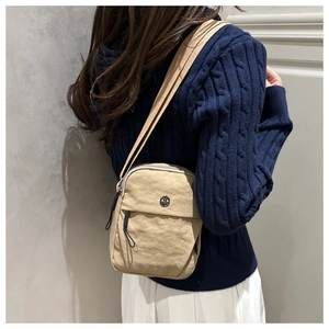 Detail of a beige nylon crossbody bag with fabric strap and circular logo on a model