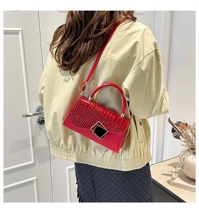 Detail view of red crocodile-textured crossbody bag with golden hardware and black buckle