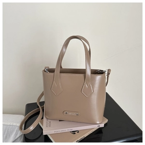 Close-up of khaki PU leather bucket bag with silver Fashion plaque on stacked books