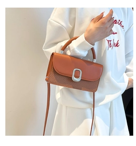 Sac bandoulière en cuir marron avec rabat et détails tressés porté par un mannequin