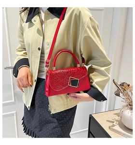 Detail of red crocodile pattern crossbody bag with a gold square clasp on a female model
