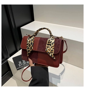 Detail of reddish-brown crossbody bag with leopard print scarf wrapped around the handle