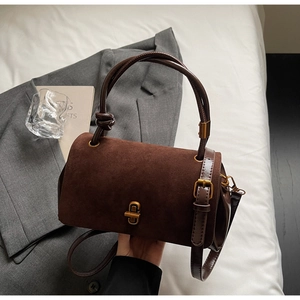 Detailed view of deep brown suede handbag with golden metal twist lock and smooth leather handle