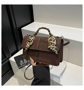 Detail of dark brown leather handbag featuring textured patchwork and leopard scarf handle