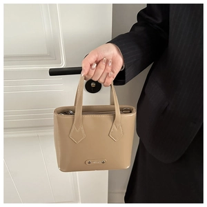 Close-up of beige leather handbag with silver Fashion plaque and slim handle details
